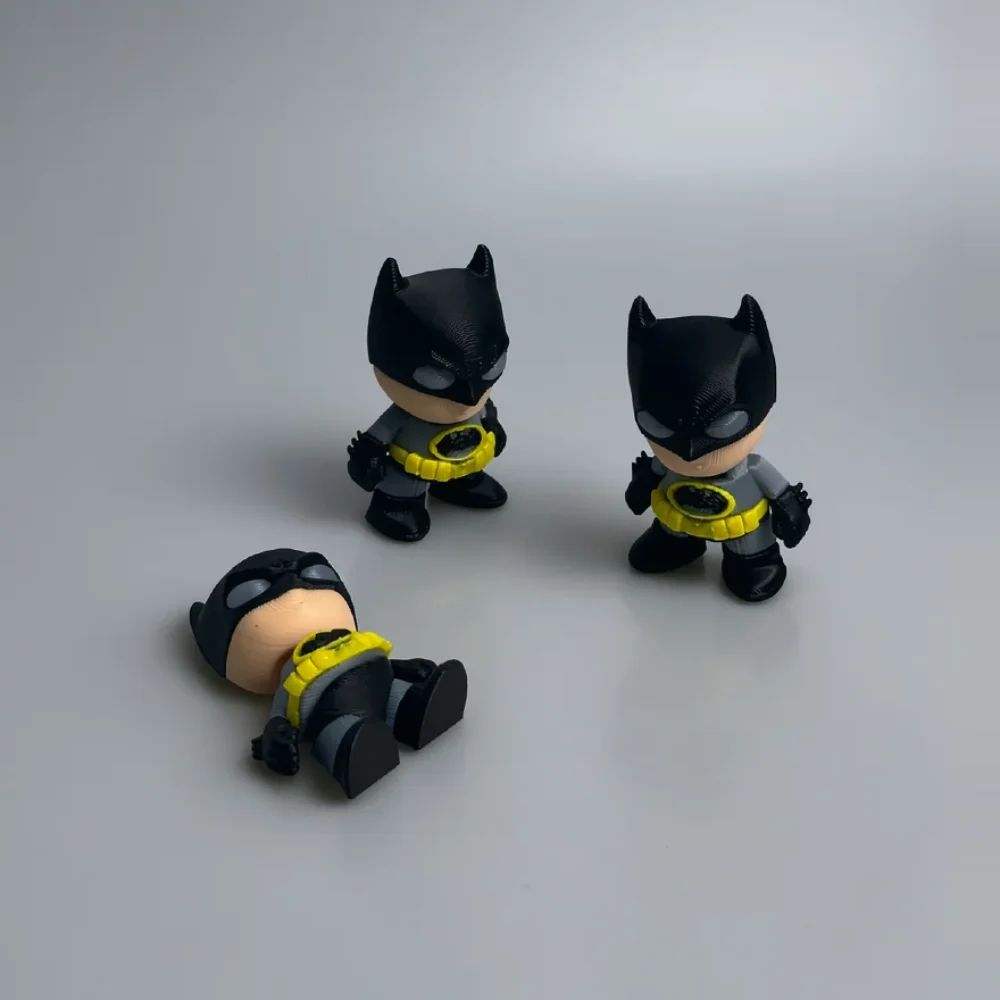 Batman: black and gray three small chibi-style Batman figurines, oversized head with black cowl and pointed ears