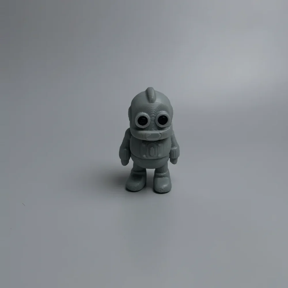 Tiny Robot: grey and black robot or astronaut figurine, rounded helmet-like head with small fin protrusion on top