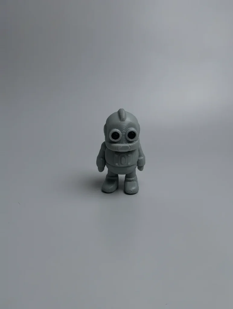 Tiny Robot: grey and black robot or astronaut figurine, rounded helmet-like head with small fin protrusion on top