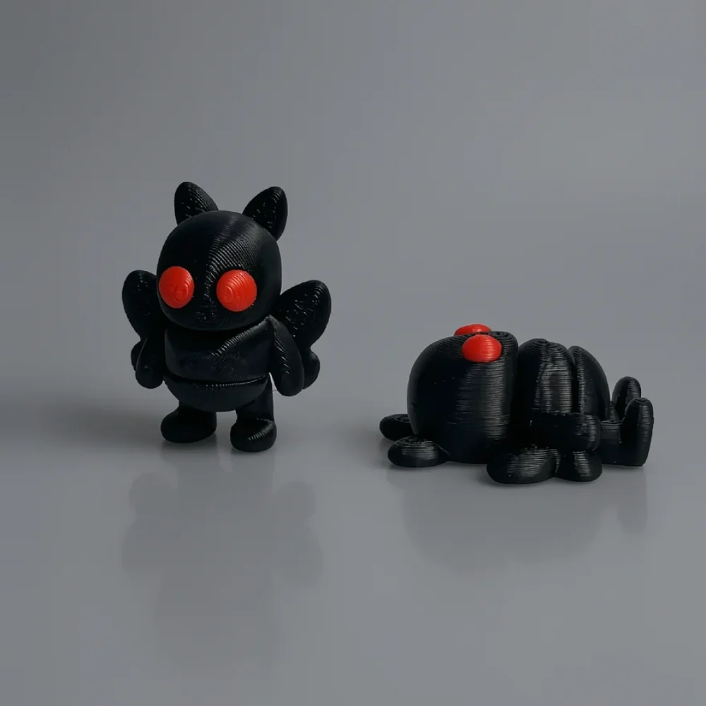 Tiny Mothman: black and red two cartoonish bat or demon figurines, large bright red circular eyes