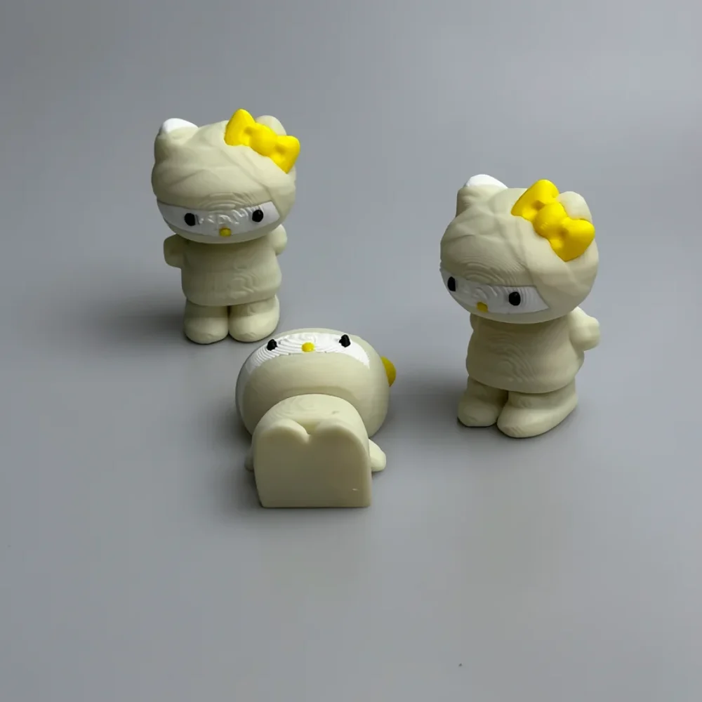 Mummy Hello Kitty: cream and yellow three Hello Kitty figurines styled as mummies, yellow bow on left ear
