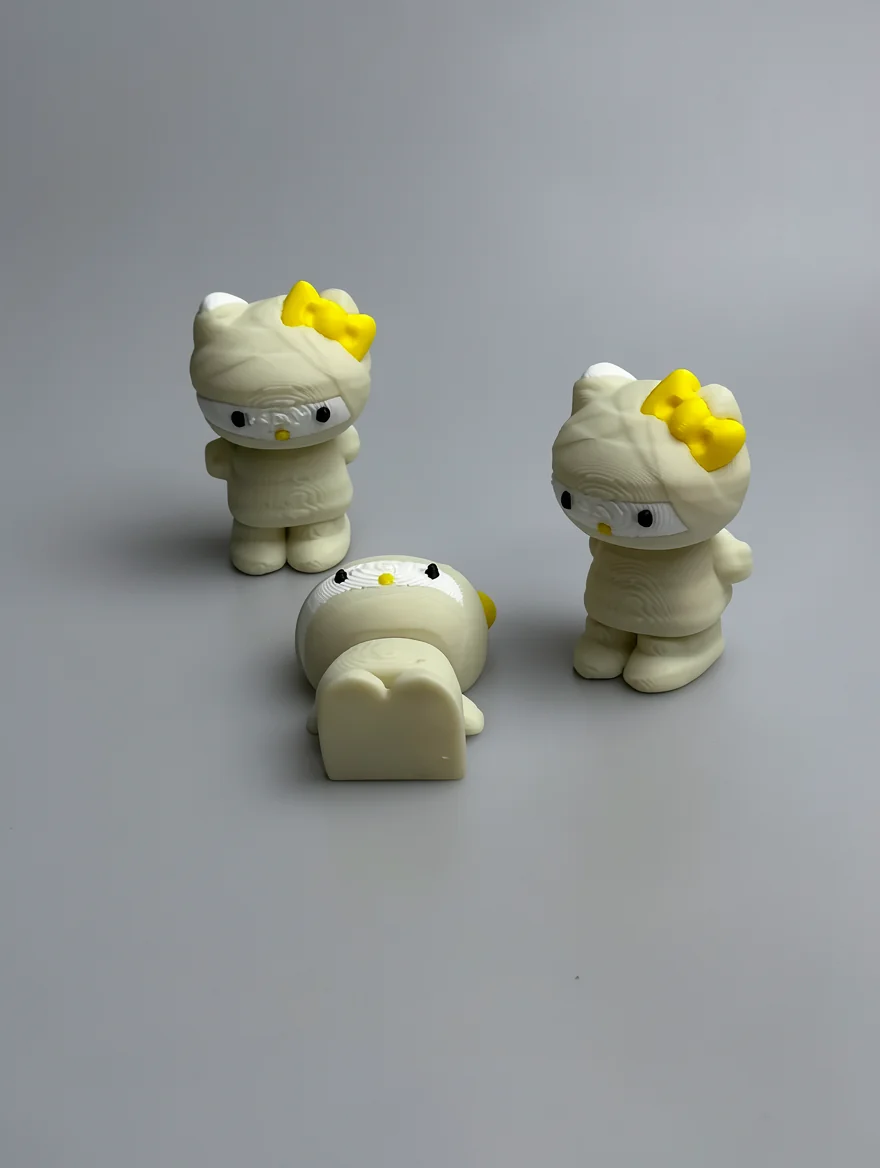 Mummy Hello Kitty: cream and yellow three Hello Kitty figurines styled as mummies, yellow bow on left ear